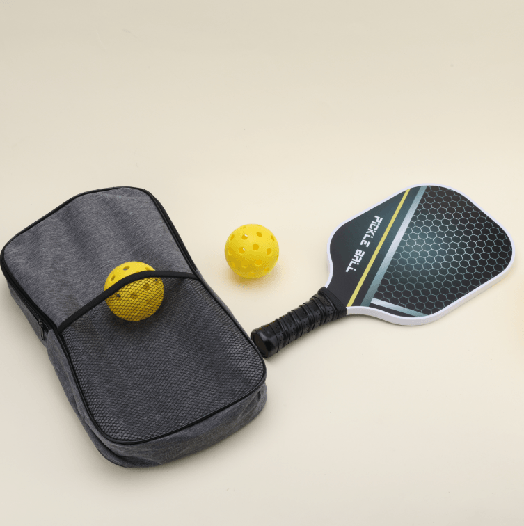 A pickleball set with two yellow hybrid pickleballs, one placed in the outer net compartment of the bag, a paddle lying flat, and the bag beside it.