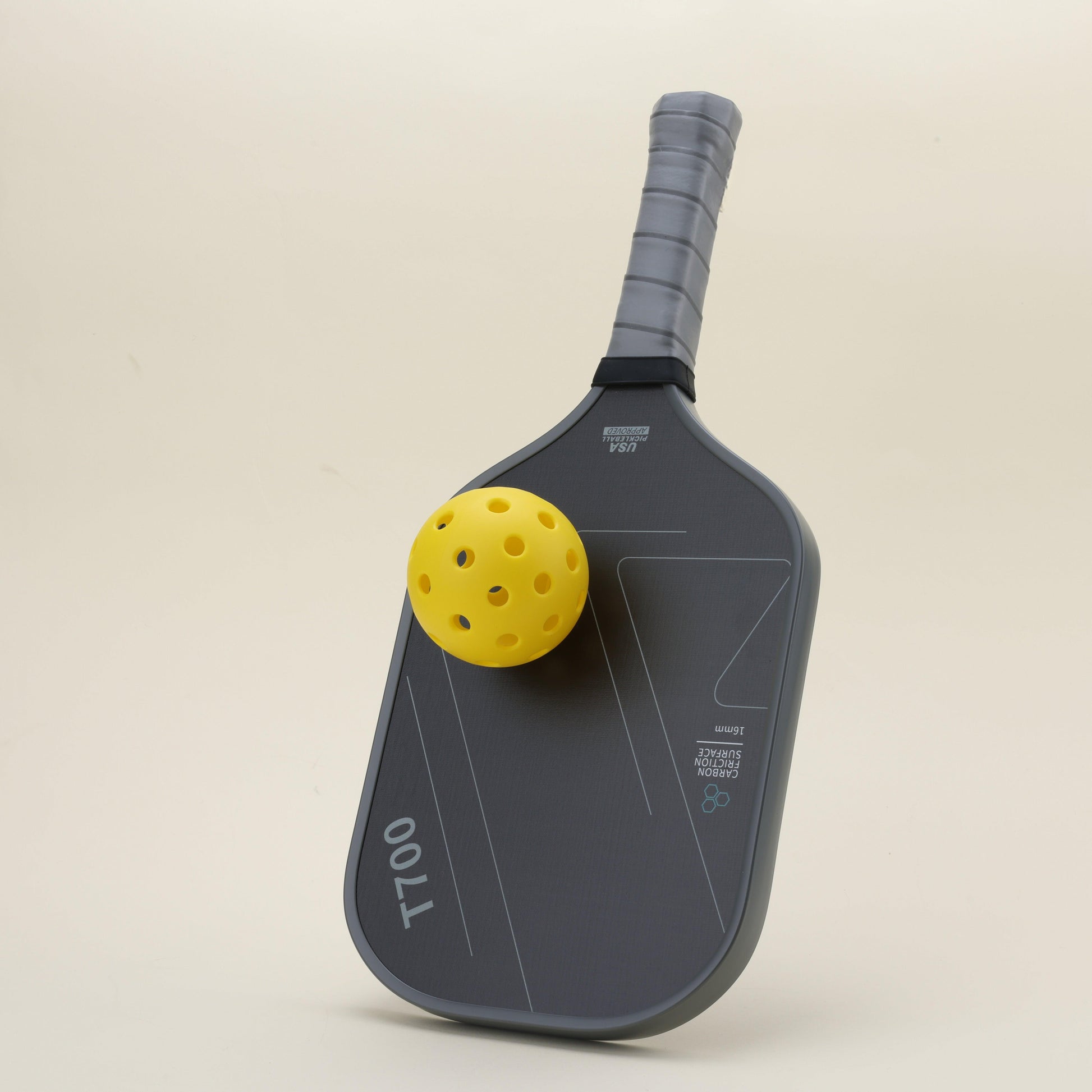 A yellow hybrid pickleball resting on a pickleball paddle featuring a sleek black-gray color scheme with geometric patterns, designed for power and control, blending modern style with functionality.