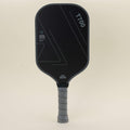Front view of a pickleball paddle with a sleek black-gray color scheme and geometric patterns, paired with a yellow hybrid pickleball resting on the surface, showcasing a blend of modern style, power, and control.