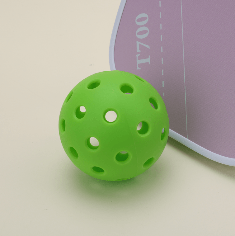 One green hybrid pickleball placed next to a T700 pickleball paddle in pink color, creating a vibrant and stylish setup.
