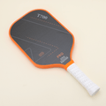 Performance pickleball paddle with a modern orange-and-black design, laying flat next to a yellow hybrid pickleball, highlighting both style and functionality.