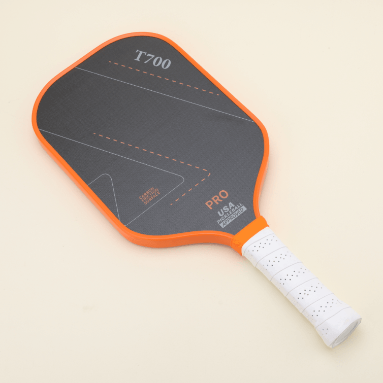 Performance pickleball paddle with a modern orange-and-black design, laying flat next to a yellow hybrid pickleball, highlighting both style and functionality.