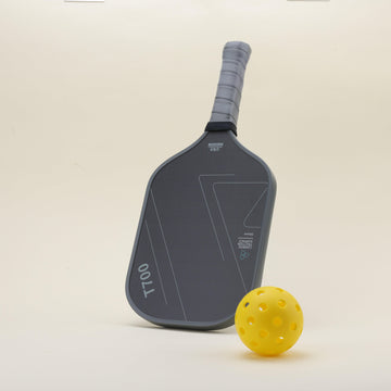Pickleball paddle featuring a sleek black-gray color scheme with geometric patterns, delivering a modern and sporty look, paired with a yellow hybrid pickleball, combining functionality with style.