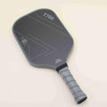 Pickleball paddle with a sleek black-gray color scheme and geometric patterns, laying flat with a yellow hybrid pickleball resting on top, showcasing a blend of modern style, power, and control.