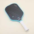 Pickleball paddle with vibrant blue representing passion and bold black conveying strength, laying on the floor next to a yellow hybrid pickleball, showcasing a striking color combination that blends style with functionality.