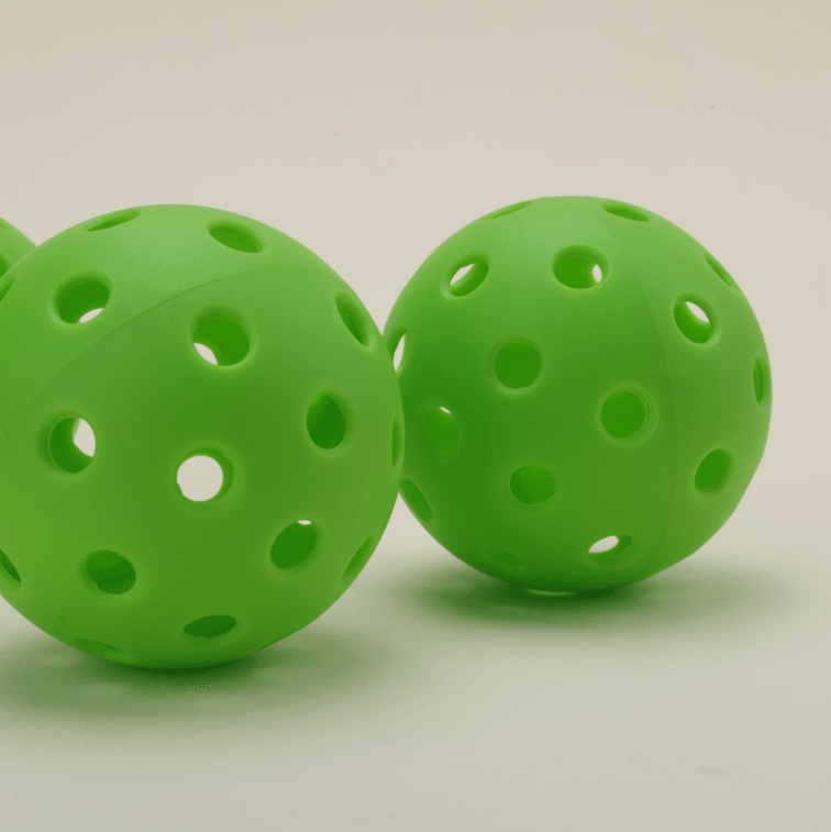Two green hybrid pickleballs resting together, showcasing their vibrant color and durable design.